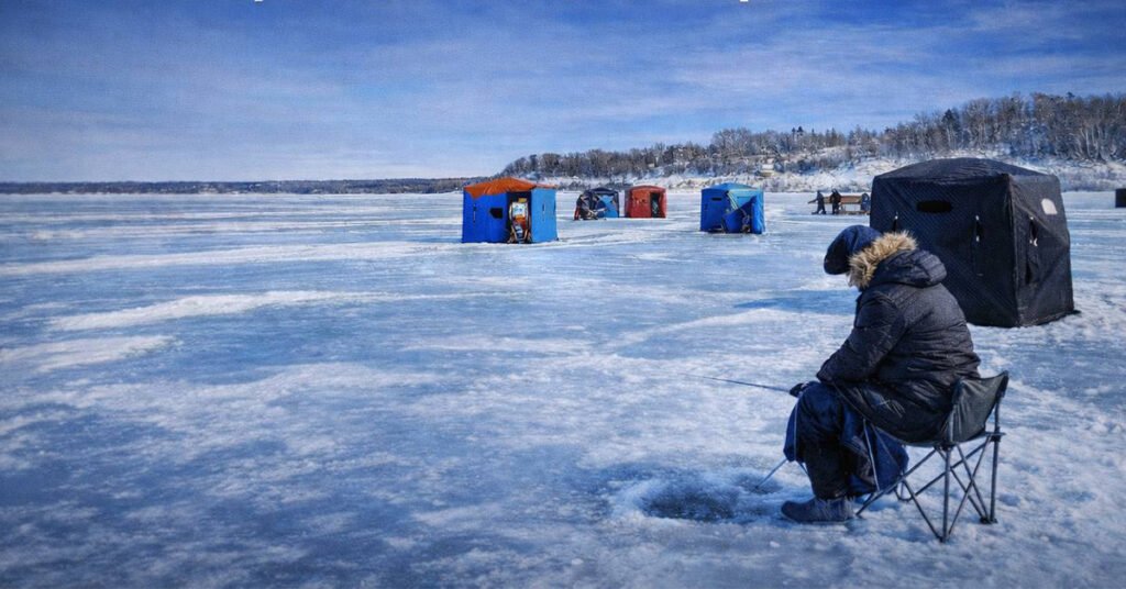 Рибалка біля синьої та чорної рибальських хатинок на замерзлому озері Сімко в сонячний зимовий день.