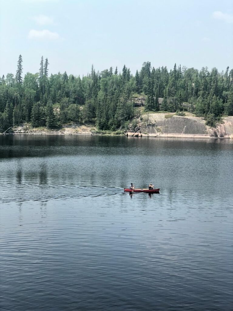 Людина веслує на каное по спокійному озеру Вест-Хок у провінції Манітоба під час заходу сонця.
