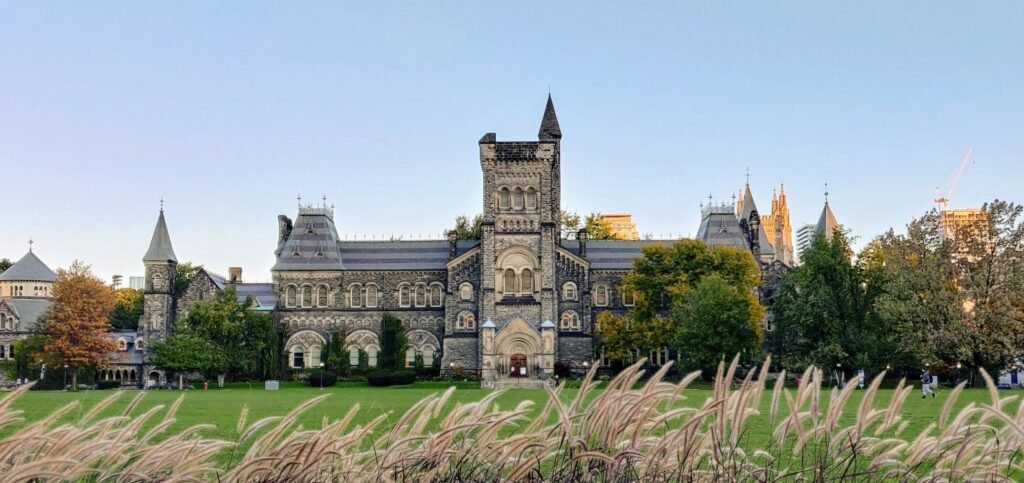 Історична будівля Університету Торонто (University College) з кам'яними вежами та зеленим газоном