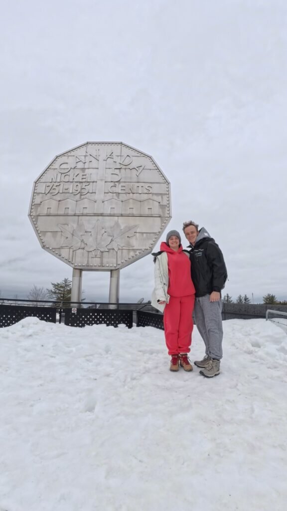 Таня Дубчак та Назар Макаренко стоять на снігу перед величезною монетою Big Nickel у місті Садбері.