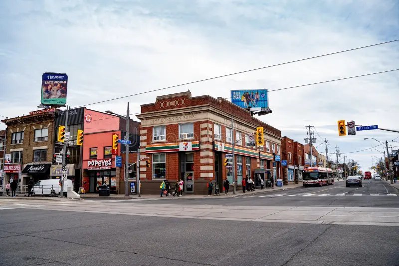 Перехрестя вулиць St. Clair Ave West та Dufferin у районі Corso Italia, Торонто: історична цегляна будівля з магазином 7-Eleven, ресторан Popeyes та міський автобус.
