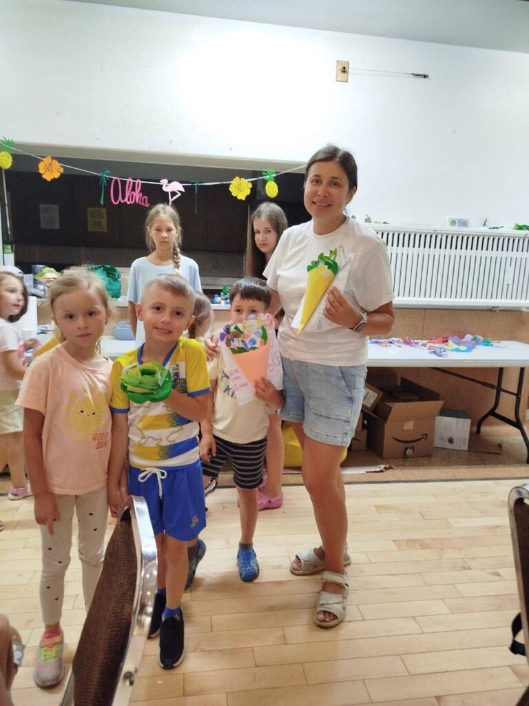 Діана Порада та діти у таборі Act&Shine тримають у руках паперові вироби на фоні декору Aloha.