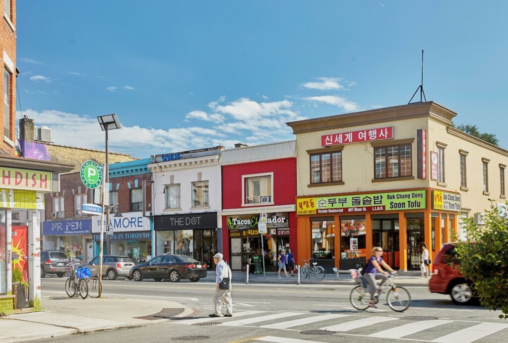 Вулиця Bloor Street у районі Koreatown у Торонто з корейськими ресторанами, вивісками та пішоходами на фоні блакитного неба.