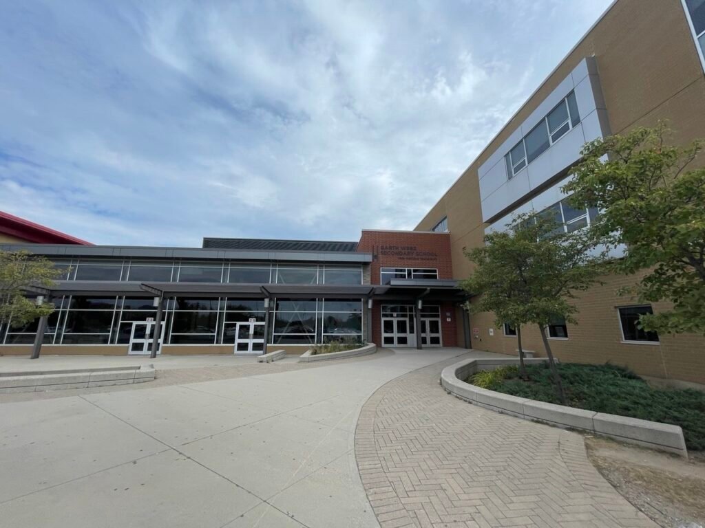 Сучасна будівля Garth Webb Secondary School в Оквілі з великими скляними вікнами та вимощеною плиткою територією перед головним входом.