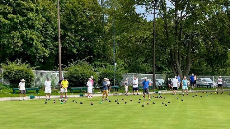 Група людей грає в боулінг на траві на великому зеленому полі Kew Beach Lawn Bowling Club у сонячний день.