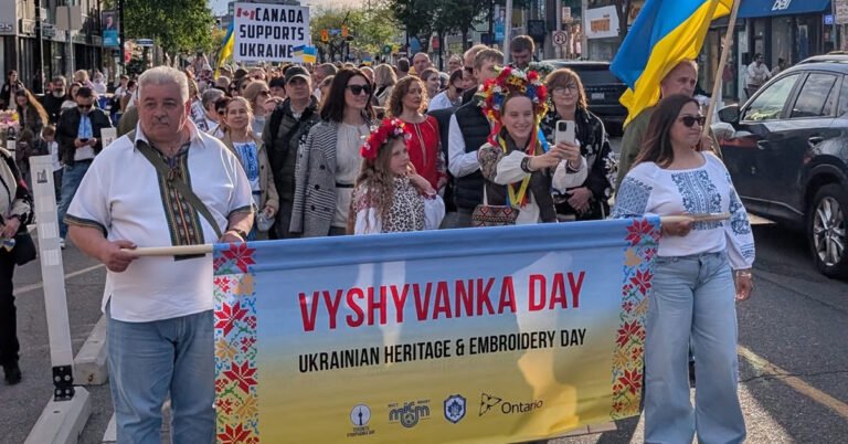 Учасники маршу в Торонто тримають банер Vyshyvanka Day попереду колони людей у вишиванках з українськими прапорами.