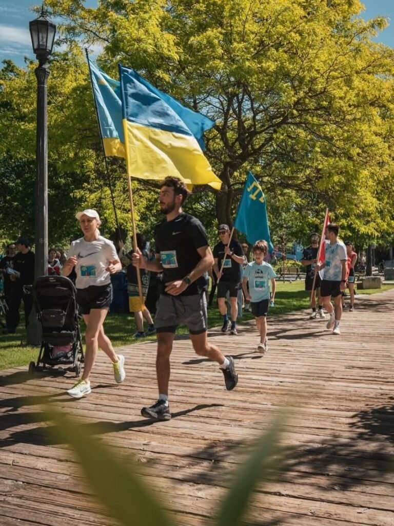 Учасники забігу в Торонто біжать дерев’яною доріжкою в парку з прапорами України та кримських татар