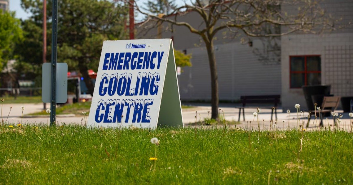 Білий інформаційний стенд-тринога з написом Emergency Cooling Centre синіми літерами на зеленому газоні в Торонто.