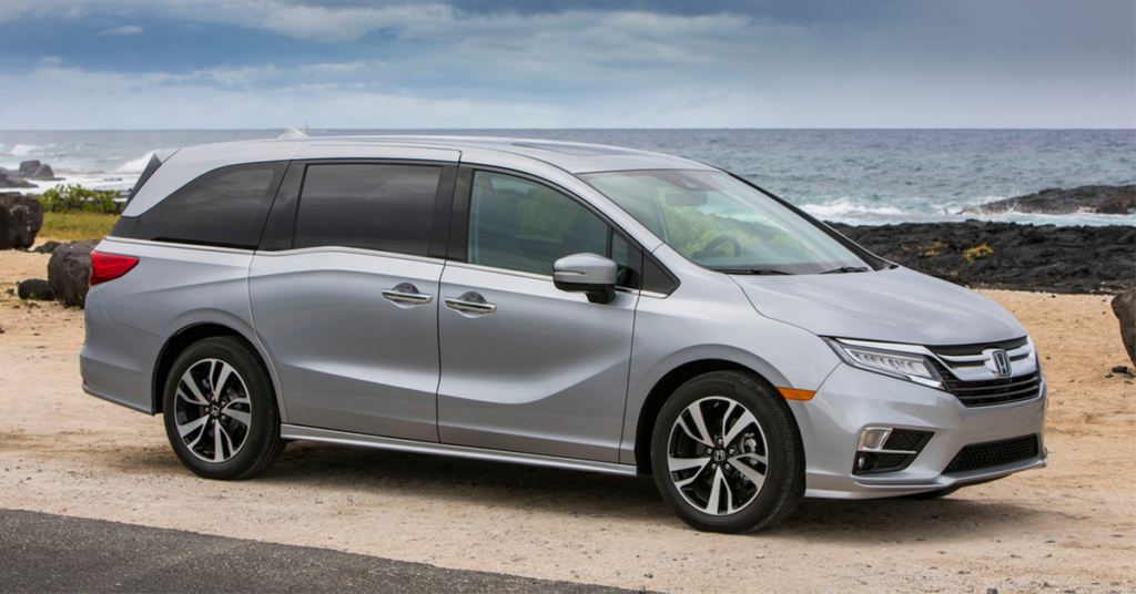 Сріблястий мінівен Honda Odyssey, припаркований на піщаному березі біля океану під похмурим небом