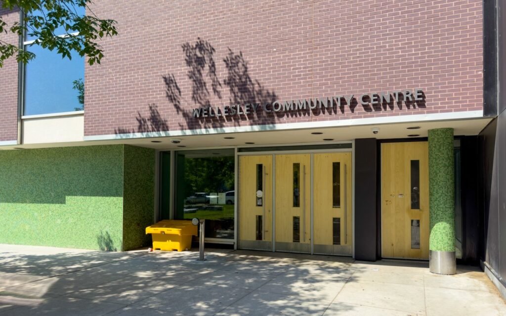 Фасад Wellesley Community Centre у Торонто з великим написом назви на цегляній стіні та дерев'яними вхідними дверима