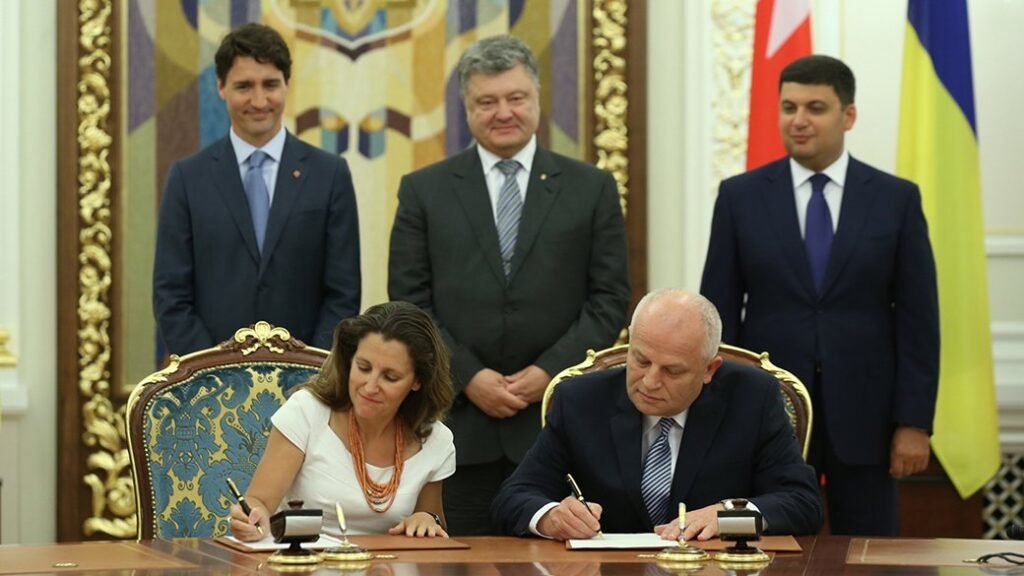 Христя Фріланд та Степан Кубів підписують документи за столом, за ними стоять Джастін Трюдо, Петро Порошенко та Володимир Гройсман на фоні державних прапорів.
