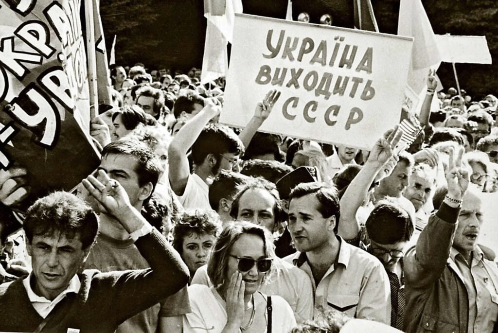 Чорно-біла фотографія масового мітингу української громади в Канаді, де люди тримають плакат із написом Україна виходить з СССР та показують жести перемоги.