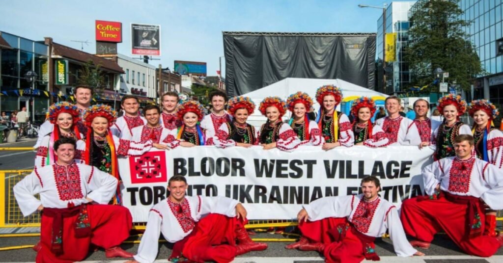Група молоді в українському національному вбранні з віночками та вишиванками тримає банер Bloor West Village Toronto Ukrainian Festival на вулиці в Торонто.
