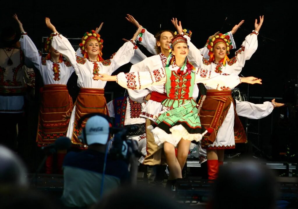 Група молодих людей у традиційних українських костюмах з вишивкою та вінках виконує народний танець на сцені під час фестивалю в Торонто.