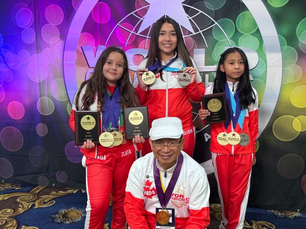 Злата Барчук у червоно-білій формі збірної Канади тримає нагороди Division Champion та медалі разом з іншими учасниками на фоні банера WCOPA.