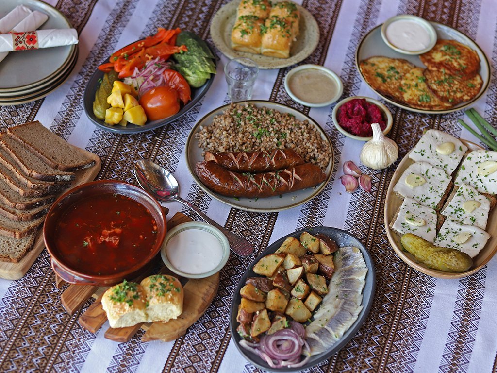Українські страви на вишитій скатертині: борщ, гречка з ковбасками, сало, оселедець та соління.