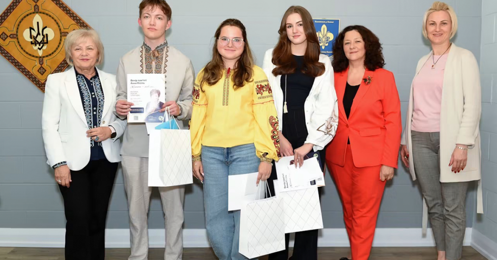 Група молодих людей та представників організації «Четверта Хвиля» на церемонії вручення стипендій імені Анни Кісіль. Студенти у вишиванках тримають сертифікати та подарунки на фоні стіни з гербом України.